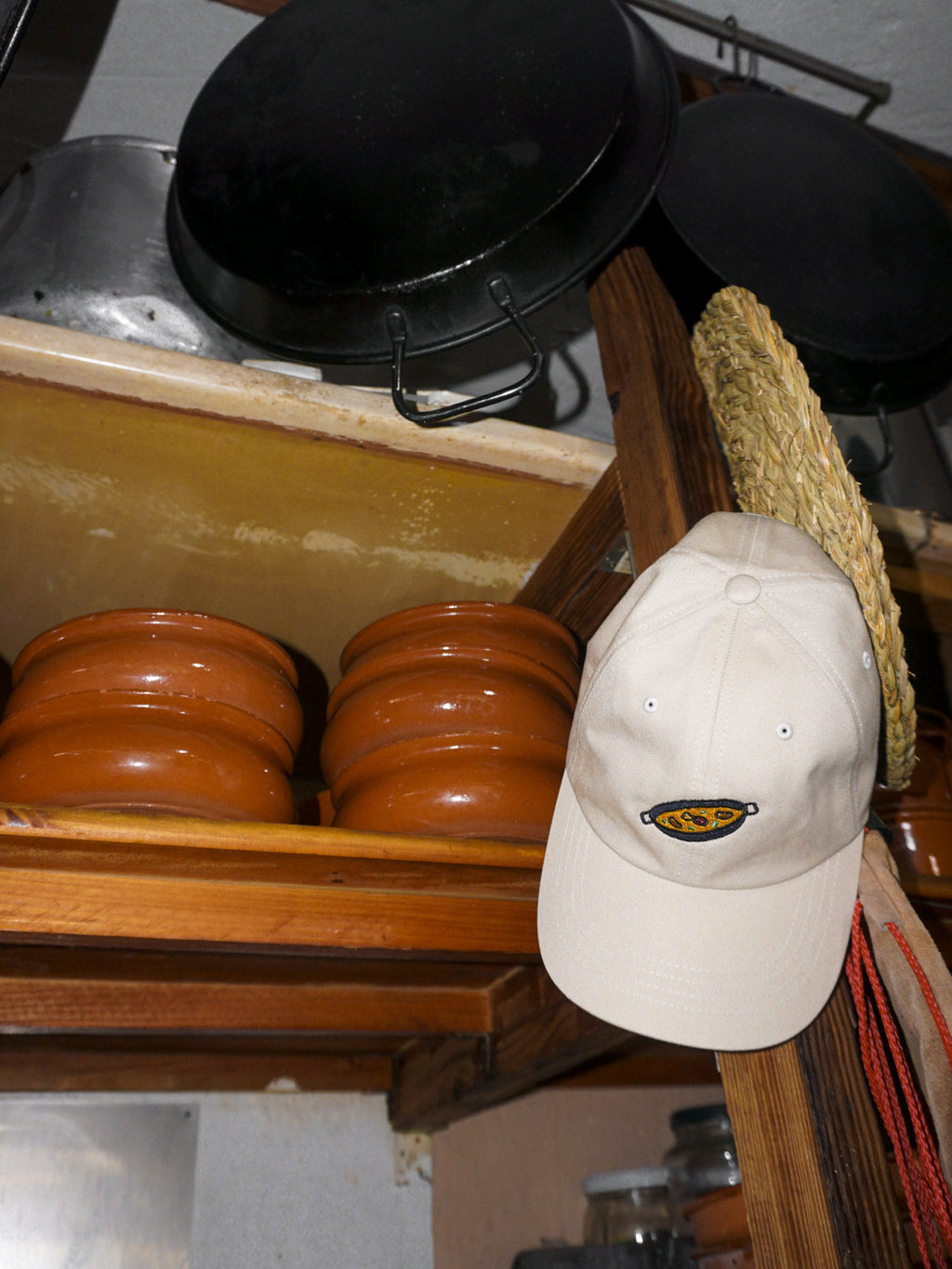Beige cap with a paella design on a wooden shelf with pots and pans