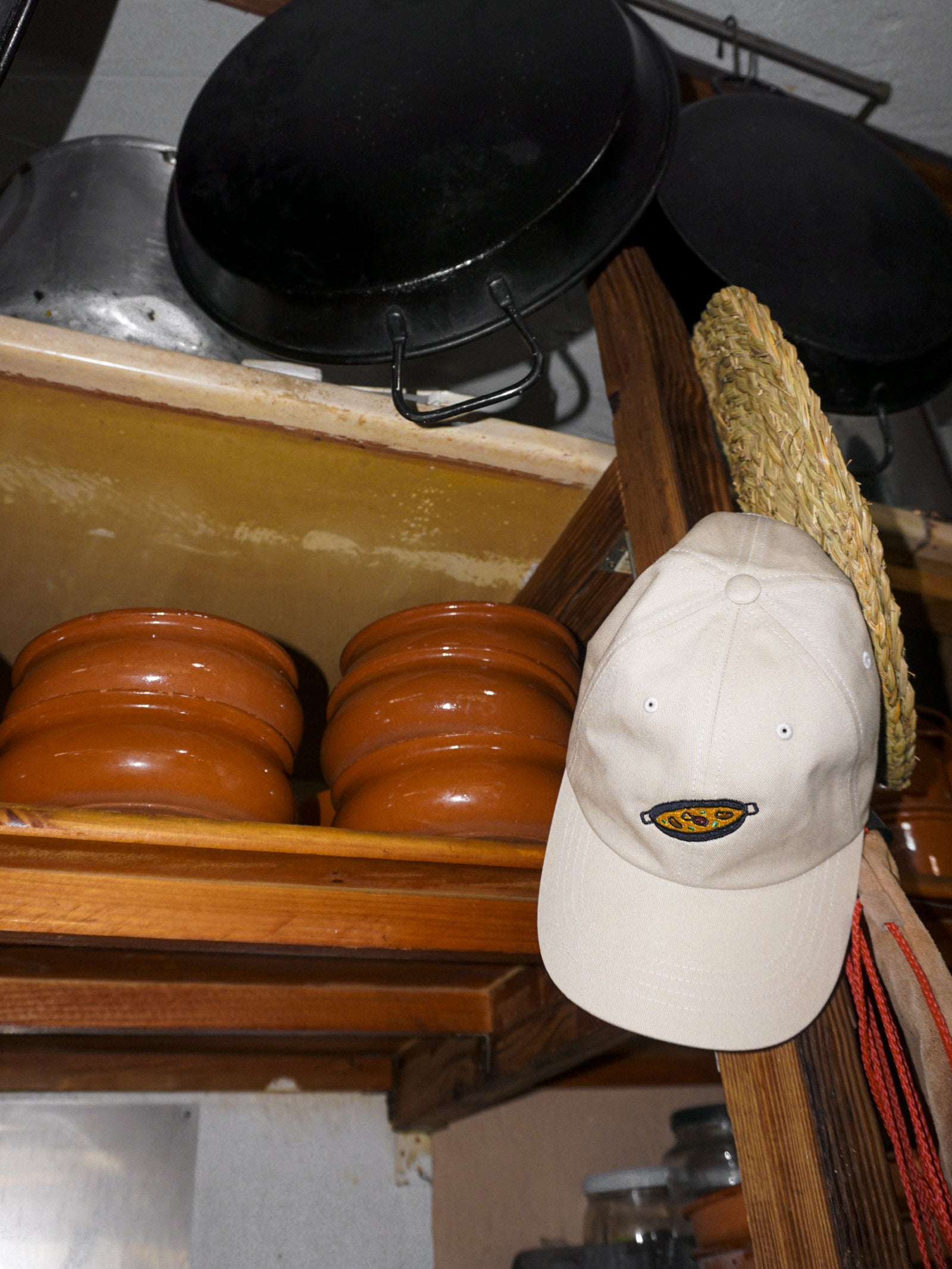 Beige cap with a paella design on a wooden shelf with pots and pans