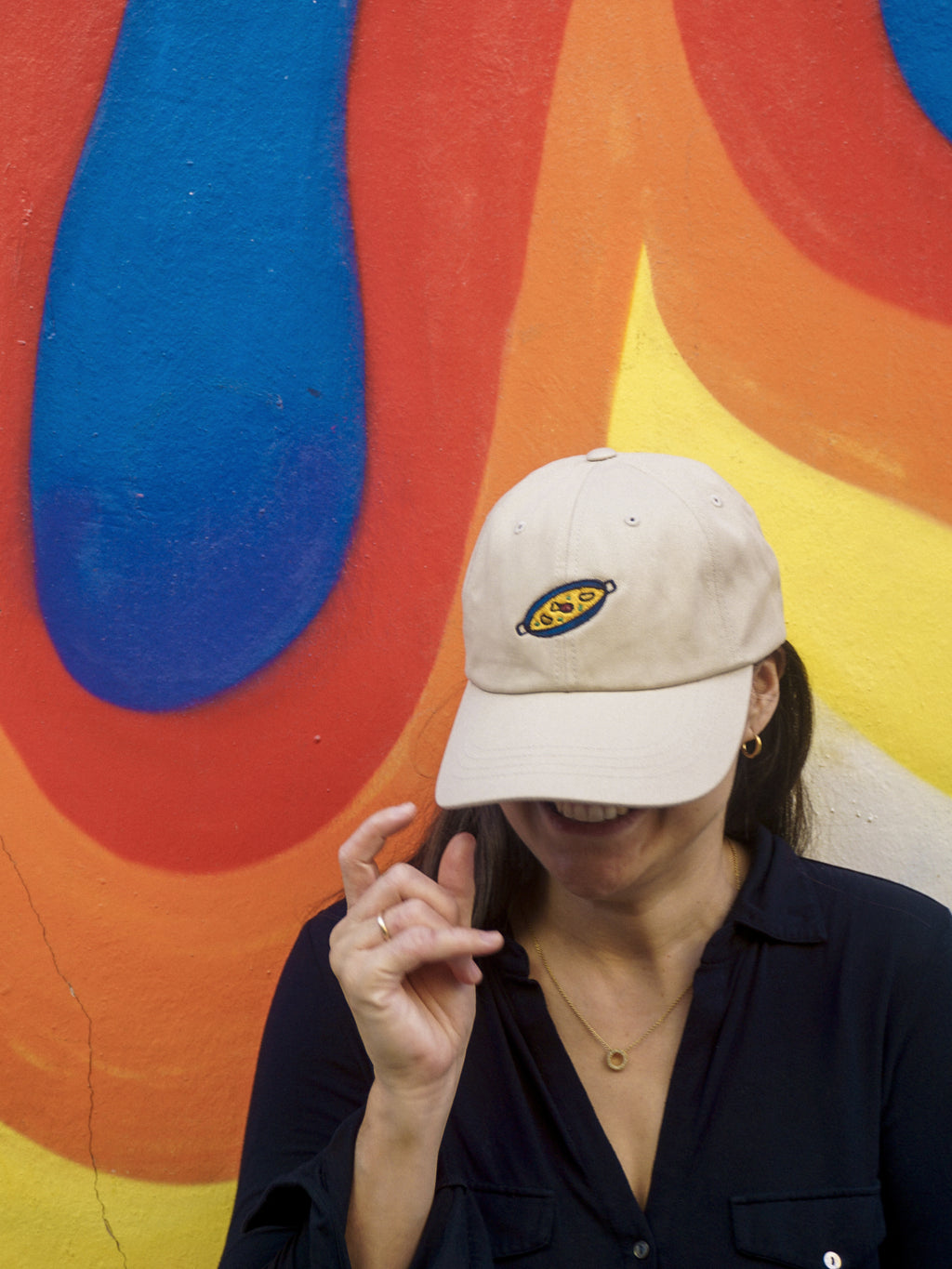 Person wearing a beige cap with a paella design against a colorful abstract background