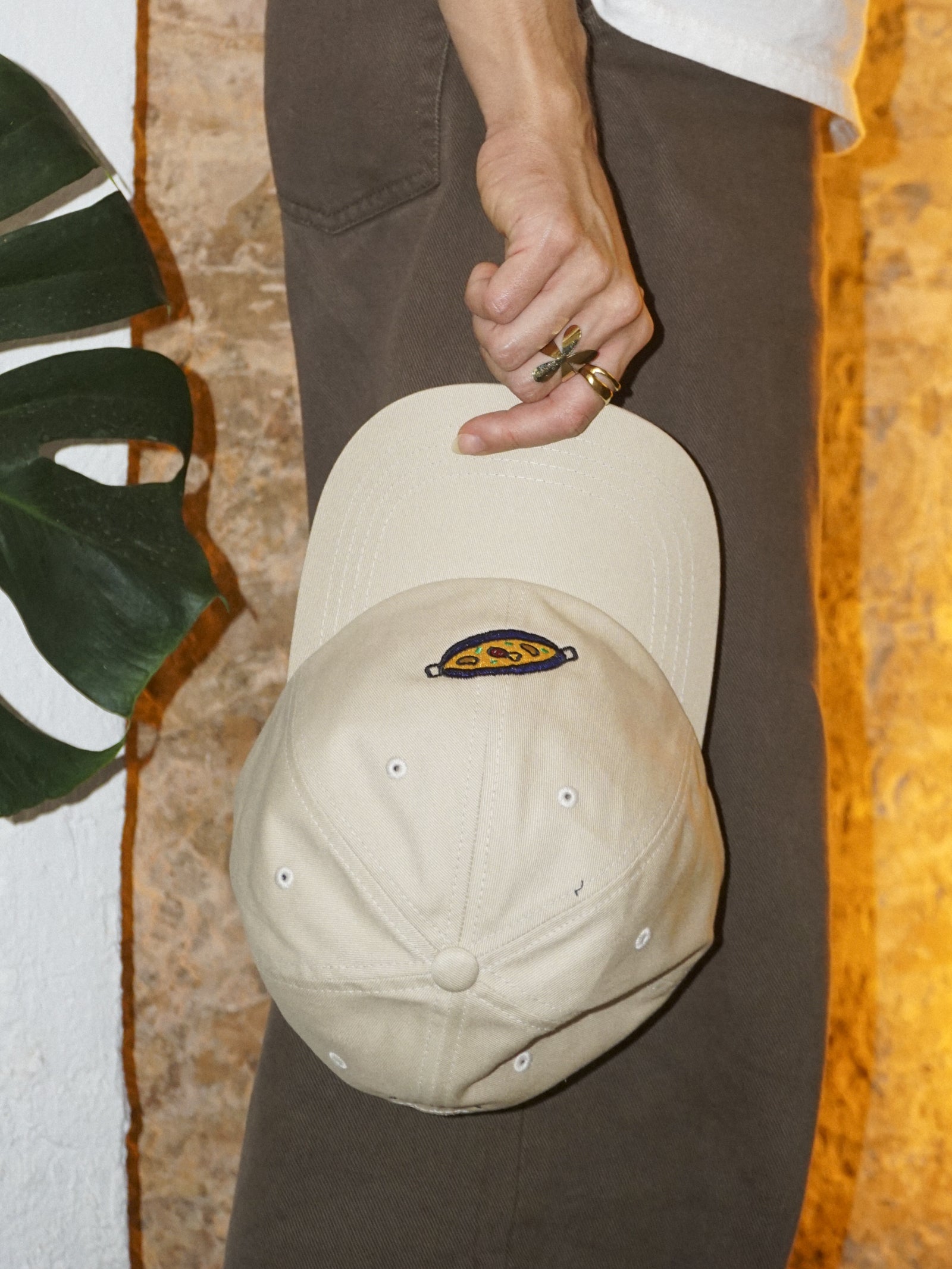 Person holding a beige cap with a paella design against a textured wall.